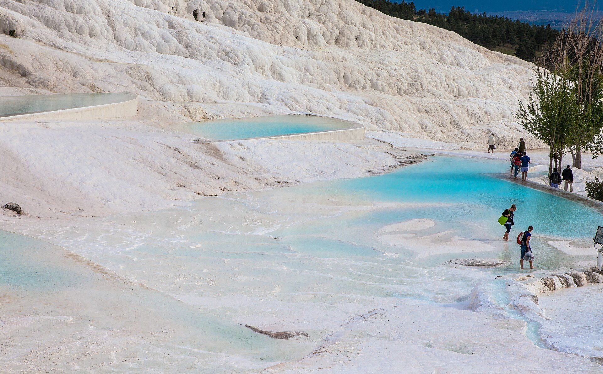 Visitors walking barefoot on the white travertine terraces and turquoise pools of Pamukkale